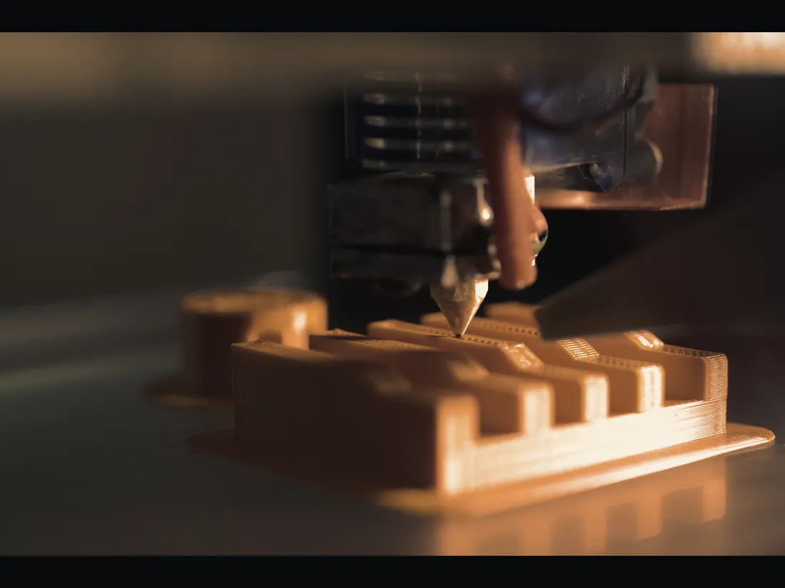Additive manufacturing nozzle building an orange structural part layer by layer.