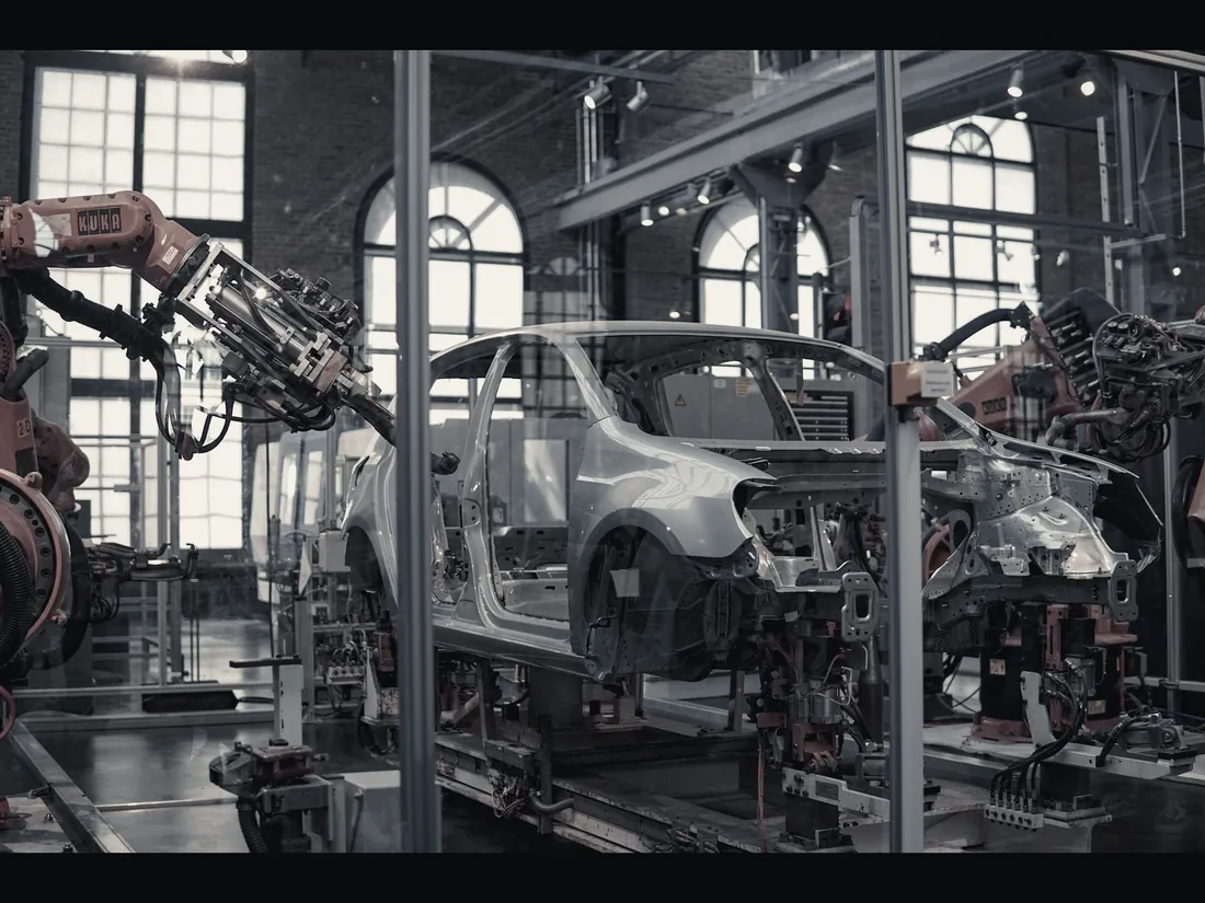 Automotive body-in-white line with industrial robot arms working on a vehicle shell.