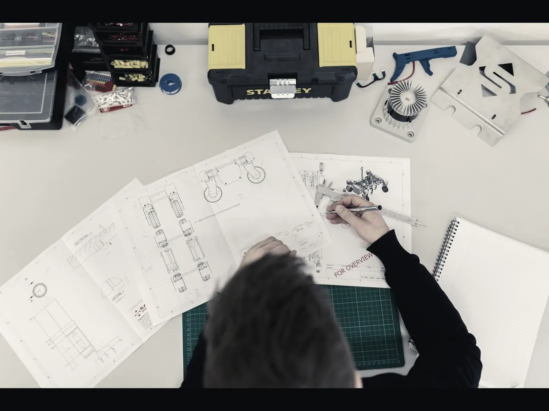 Engineer's desk with hand-drawn mechanical schematics, calipers and component sketches for the Gen-3 limb assembly.